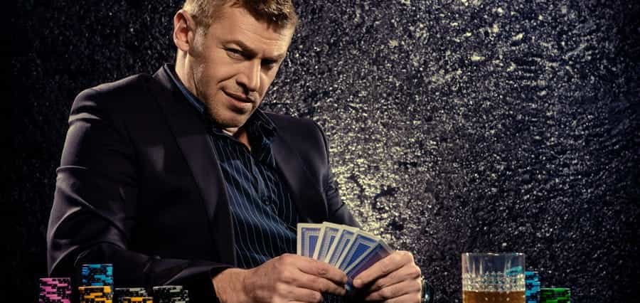 A man looking at the camera while holding a hand of cards.