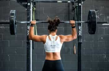 A female bodybuilder lifts weights from behind.