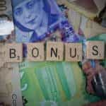 Scrabble tiles spell out the word bonus while being placed on top of currency notes.