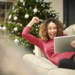 A smiling and happy lady celebrates a winner while watching an event on her tablet led on the sofa.