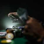 A person’s hands playing a pair of poker chips during a game of poker at a physical poker table.