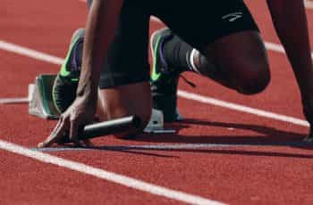 A runner in the ready position at the start line of an outdoor track and field racetrack.